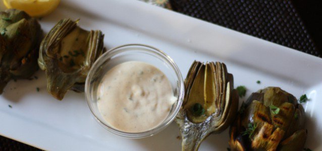 Grilled artichokes served on a white platter with remoulade dipping sauce