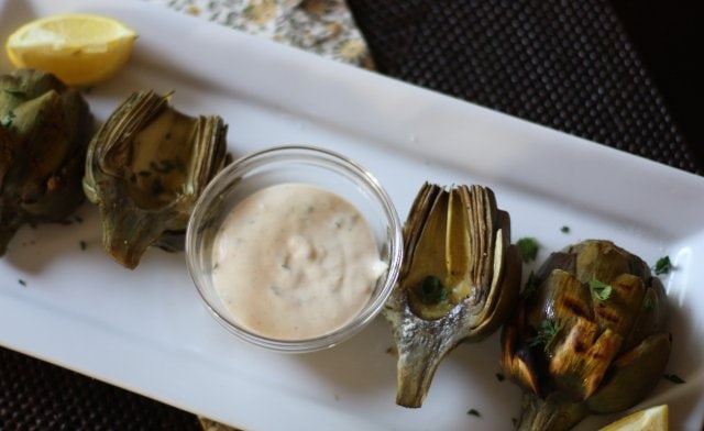 Grilled artichokes served on a white platter with remoulade dipping sauce