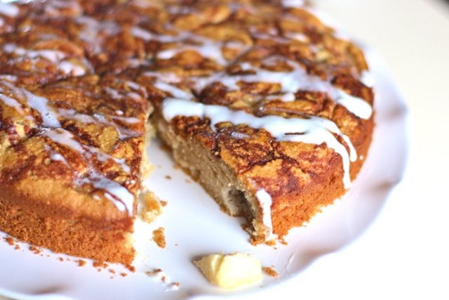 apple spice coffee cake with one piece remove on a white plate and frosting drizzled on top