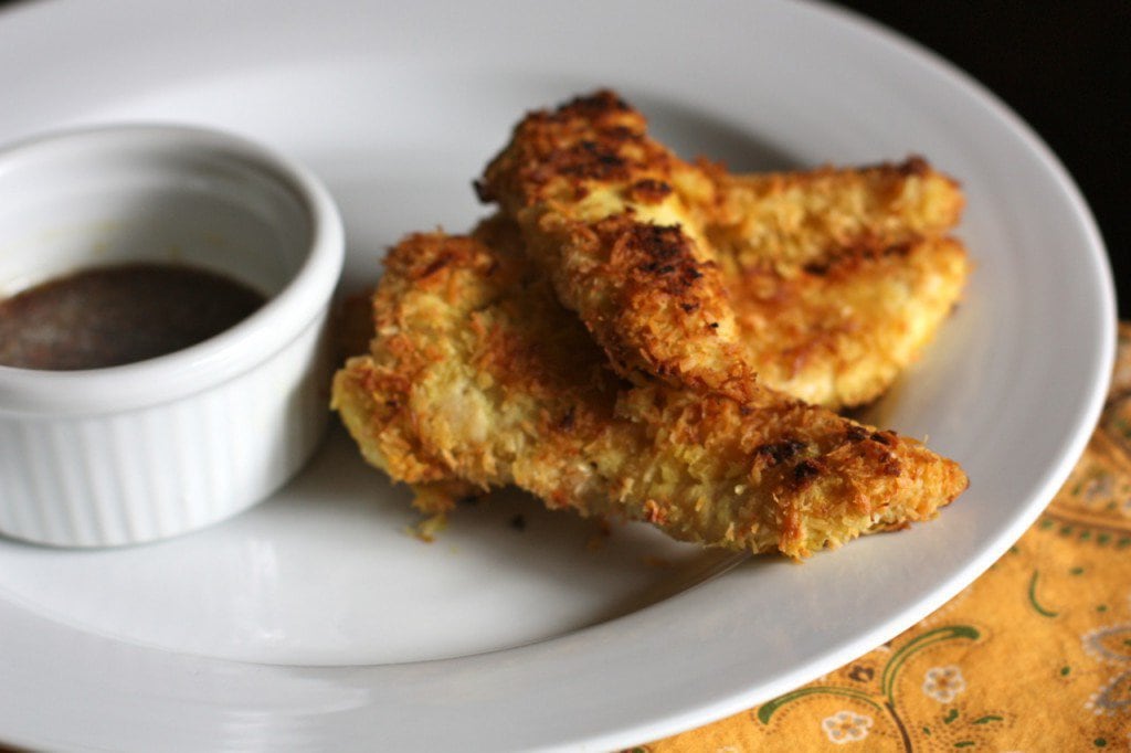 baked gluten free chicken strips on a white plate with honey mustard sauce in a ramekin next to it