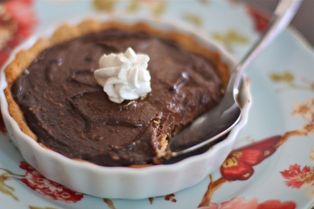 vegan chocolate pudding pie with a bite out of it in a smaller pie plate and a spoon coming out