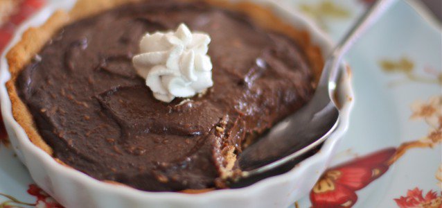 vegan chocolate pudding pie with a bite out of it in a smaller pie plate and a spoon coming out