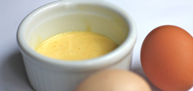 easy hollandaise sauce in a ramekin with two eggs next to it