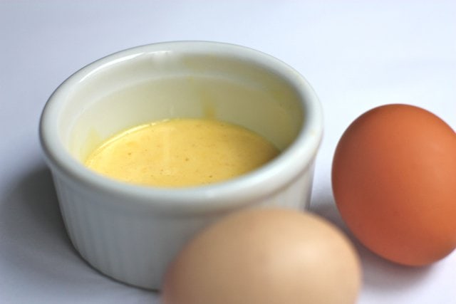 easy hollandaise sauce in a ramekin with two eggs next to it