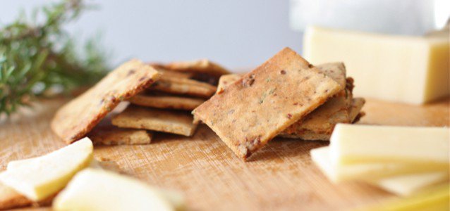 savory and sweet crackers on a cheese board with cut cheese right next to it and a sprig of rosemary in the background