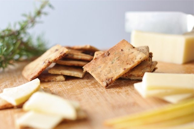 savory and sweet crackers on a cheese board with cut cheese right next to it and a sprig of rosemary in the background