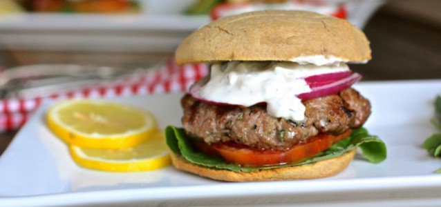 A Greek gyro burger topped with tomato, onion and a creamy cucumber yogurt sauce.