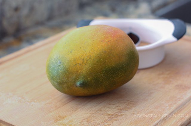 how to peel a mango using an oxo slicer in the background with an intact mango in the foreground