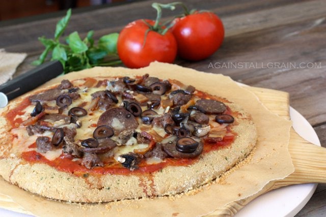 gluten free meat lovers pizza on a cutting board with tomatoes in the background