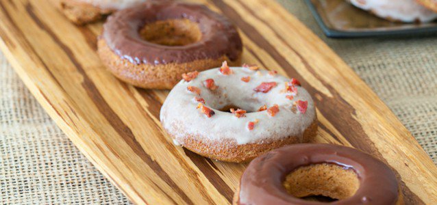 A display of baked pumpkin spiced doughnuts some with chocolate frosting and others with maple vanilla frosting with bacon sprinkles.