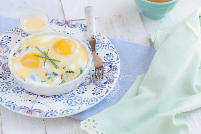 A ramekin of Baked Eggs with Bacon, Greens, and Hollandaise.