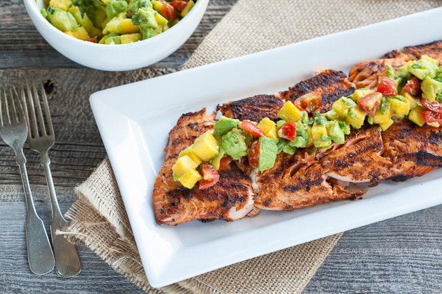 blackened grilled salmon on a white plate with a mango-avocado salad on top