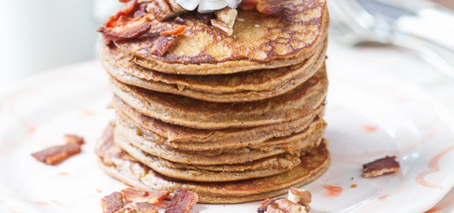 A stack of delicious spiced pumpkin pancakes topped with cooked bacon, chopped pecans and whipped cream.