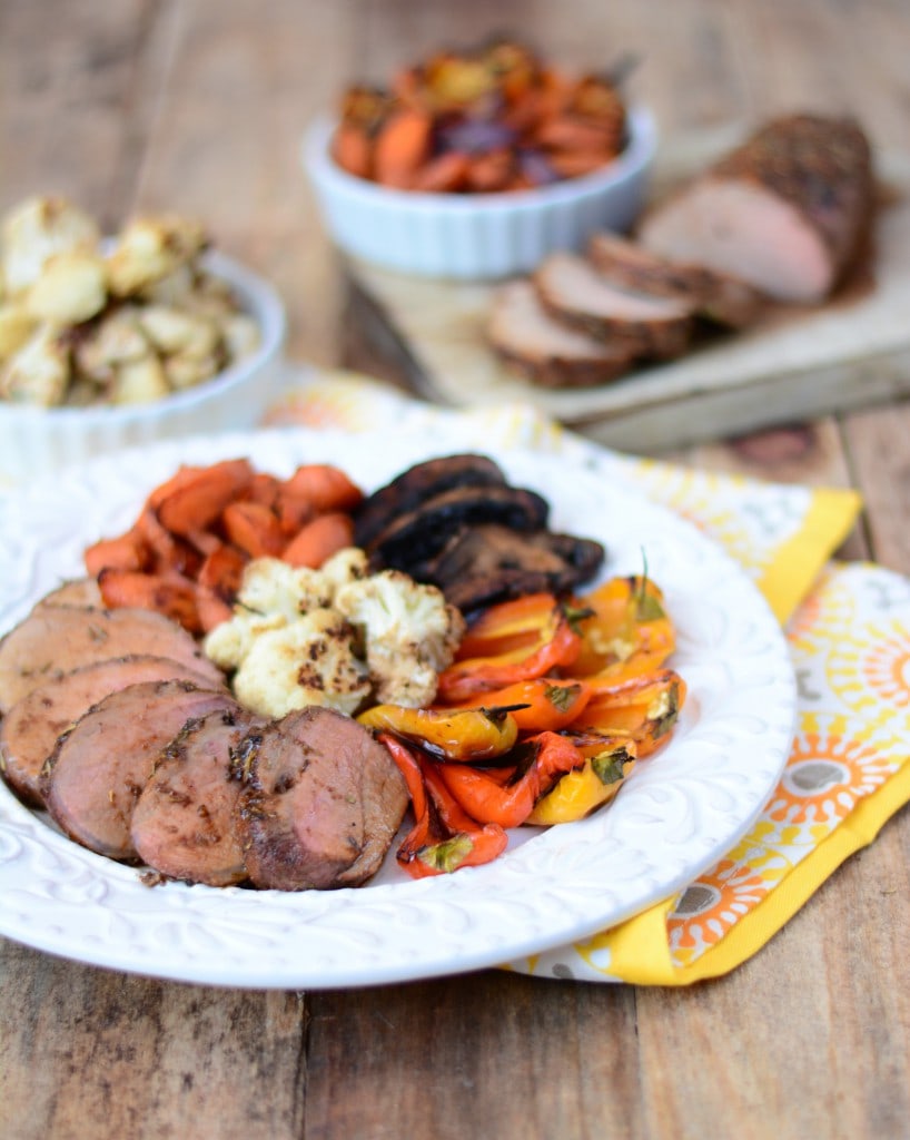 maple ternderloin served on a white plate surrounded by a variety of roasted vegetables