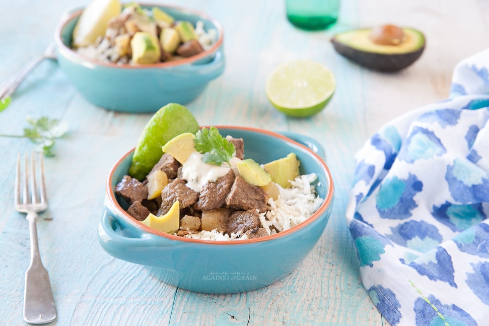 Crockpot Mexican Stew served over cauliflower rice and a side of fresh avocado. Served in a blue bowl on a light blue wooden table. 