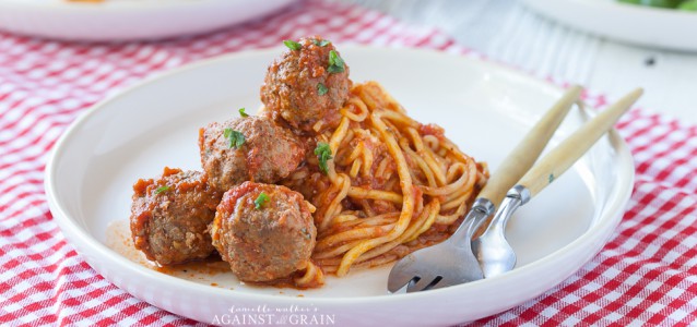 gluten free spaghetti and meatballs on a plate with a fork and knife over a checked tablecloth