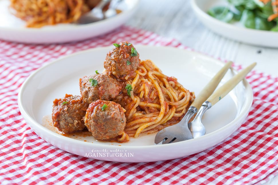 gluten free spaghetti and meatballs on a plate with a fork and knife over a checked tablecloth