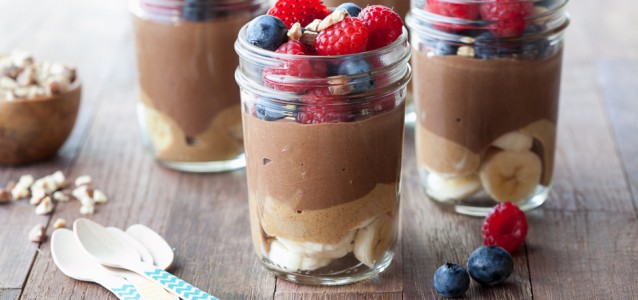 4 mason jars filled with chia/chocolate pudding with almond butter and bananas on bottom and fresh berries on top.