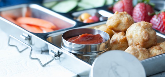A lunch box filled with chicken nuggets, veggies, fruit and a container of homemade paleo ketchup. The ketchup is sweetened with dates and kid approved!