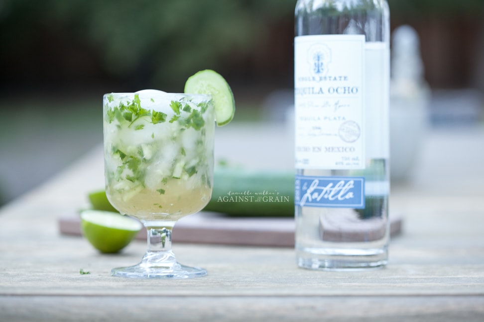 healthy margarita with cucumber and cilantro in a goblet with a lime and a bottle of tequila on the side