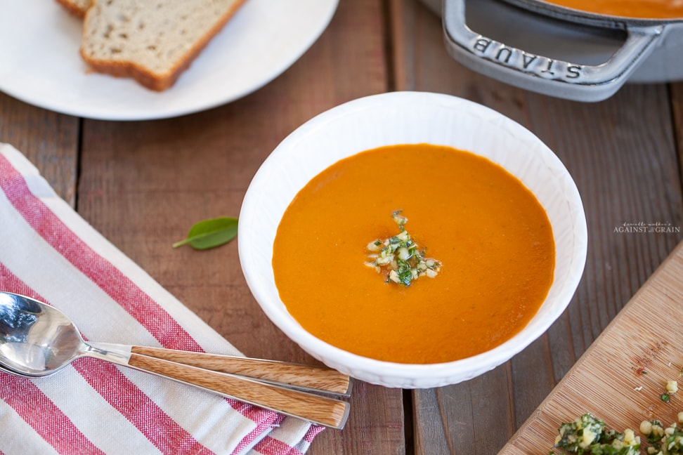 A bowl of steaming creamy tomato soup topped with pesto gremolata.