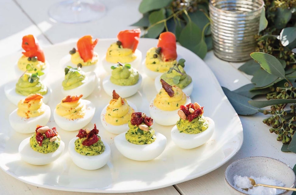 A tray of 4 different deviled eggs, Smoked Salmon and Dill, Avocado Tarragon, Pesto with Sun-dried Tomatoes, and Truffled Bacon