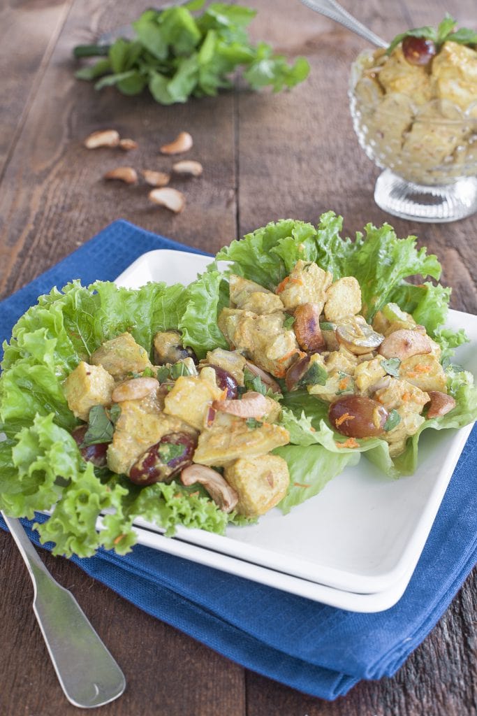 Curry Chicken Salad served on lettuce leaves on a white plate placed on a wooden table