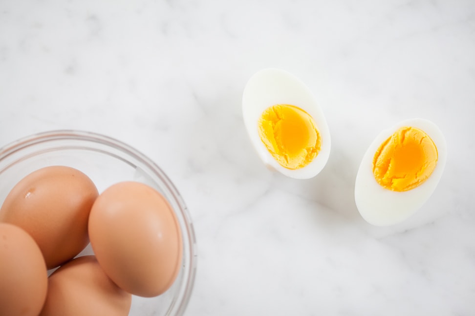 instant pot hardboiled eggs with one cracked and halved outside of a bowl showing the yolk