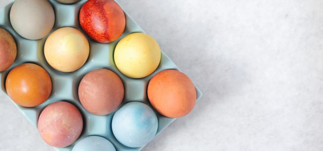 A tray of naturally dyed Easter eggs in hues of blue, yellow, orange and red.