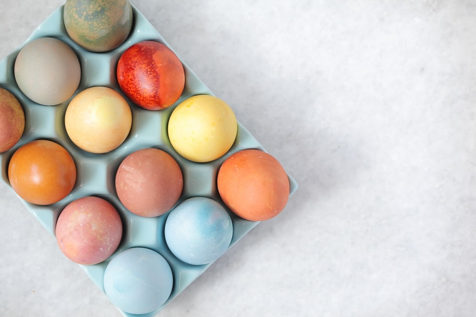 A tray of naturally dyed Easter eggs in hues of blue, yellow, orange and red.