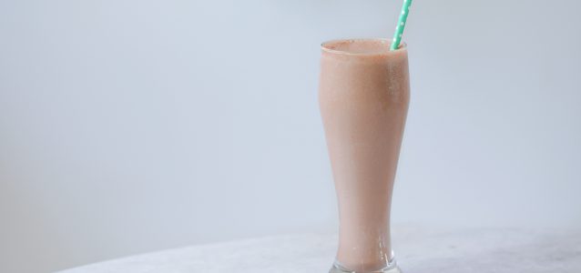 chocolate paleo protein shake in a glass with a green straw coming out of it