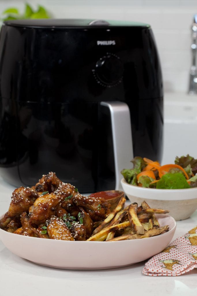 Sticky Sesame Chicken Wings with french fries in a white plate next to a black air fryer