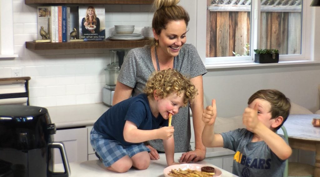 Mother stands in home kitchen with her two sons while they enjoy a plate of air fried french fries