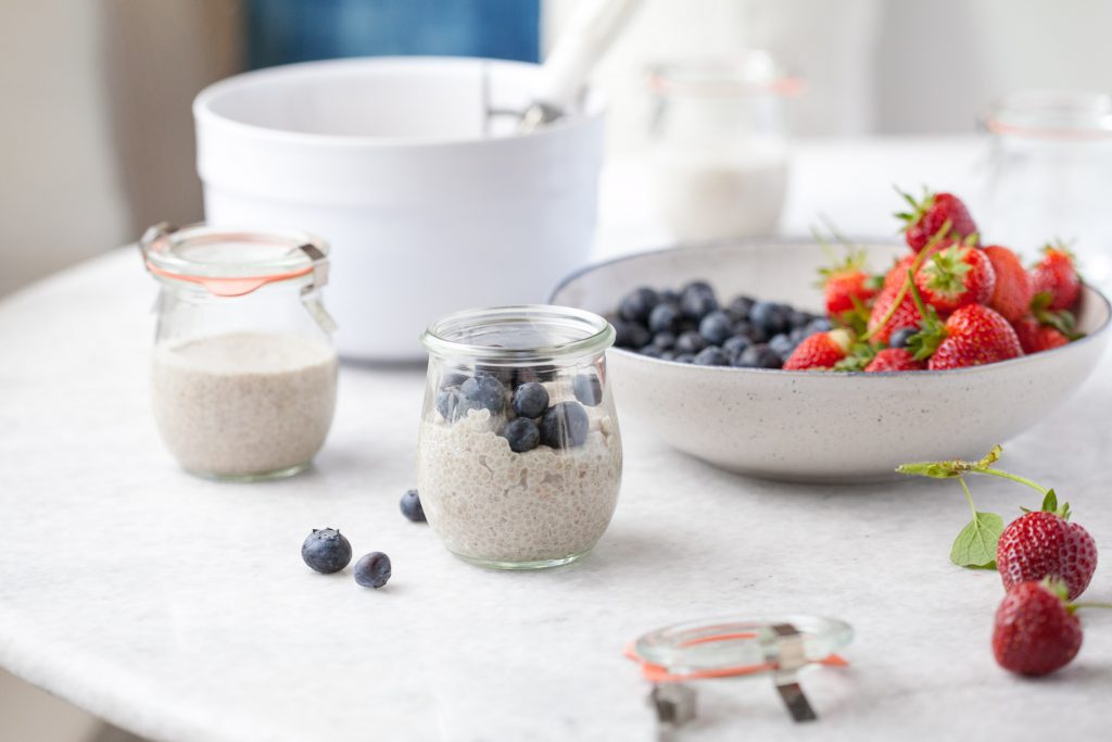 dairy free vanilla chia pudding in a small glass jar with blueberries on top on a table with fresh berries next to it