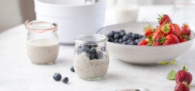 dairy free vanilla chia pudding in a small glass jar with blueberries on top on a table with fresh berries next to it