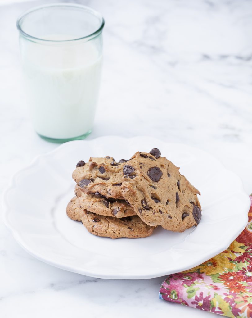 nut-free chocolate chip cookies on a white plate on a marble counter next to a glass of milk 