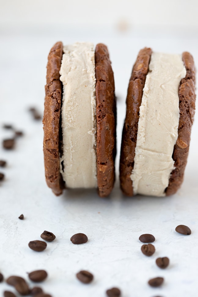 brownie cookies with a coffee ice cream middle displayed side by side on a white counter with whole coffee beans