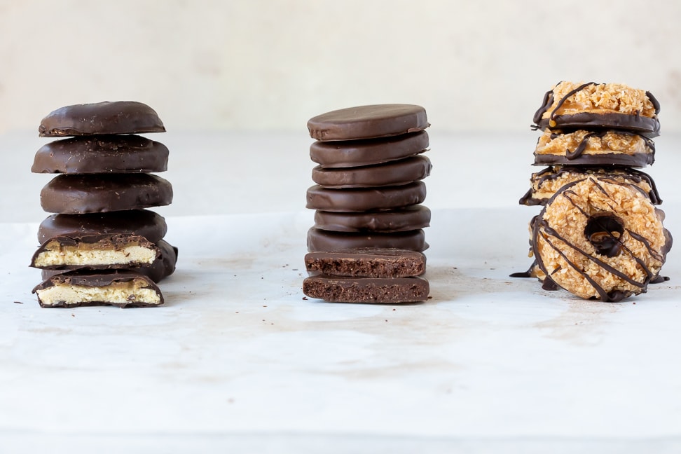 stacks of thin mint, tagalong and samoa cookies on a white surface with one cookie placed in front of stack for display