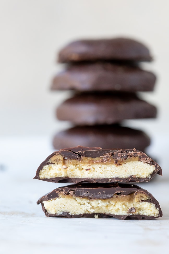 a tagalong cookie cut in half with a stack of the chocolate covered cookies in the background; all on a white surface