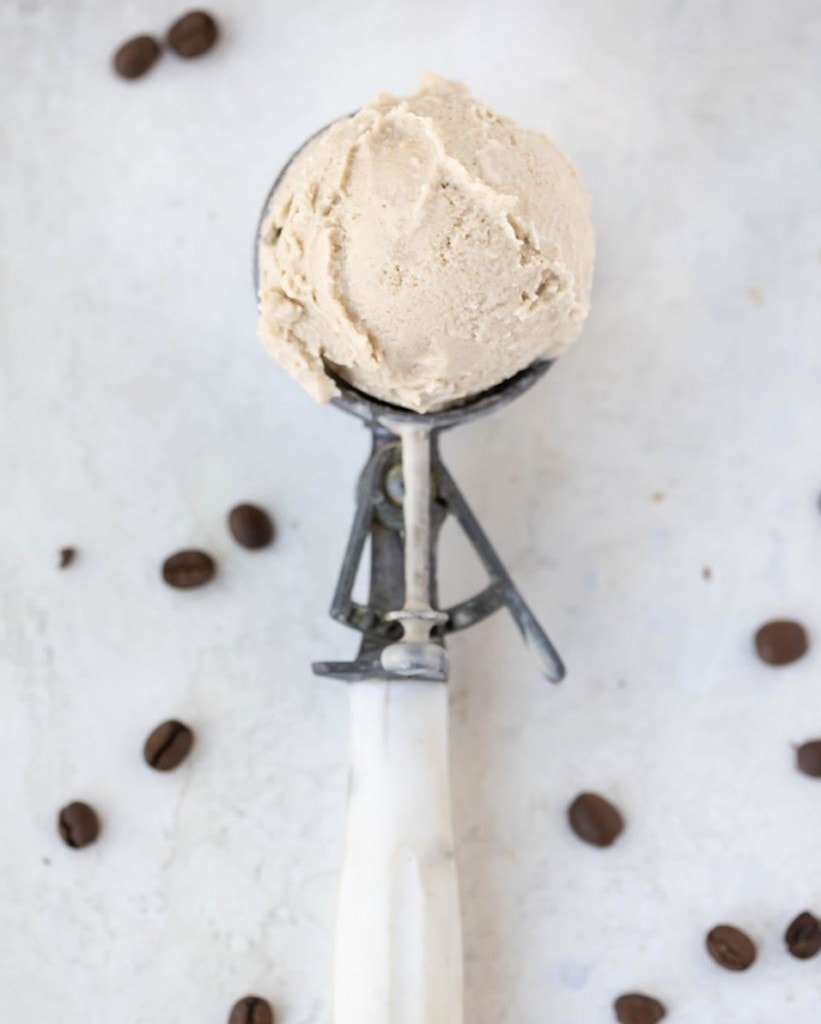 Ice cream in an ice cream scoop on a white counter surrounded by coffee grains