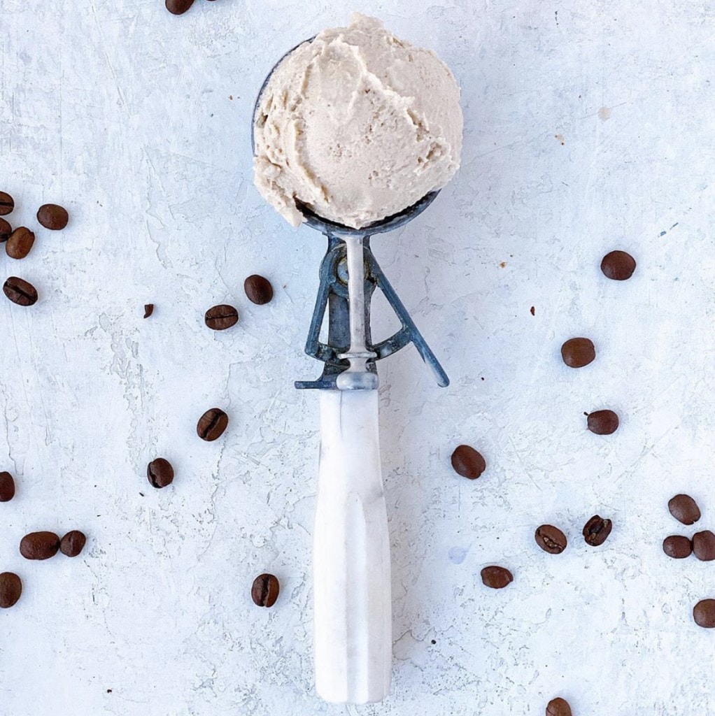 ice cream in a white ice cream scoop laying on a white marble counter sprinkled with coffee grains