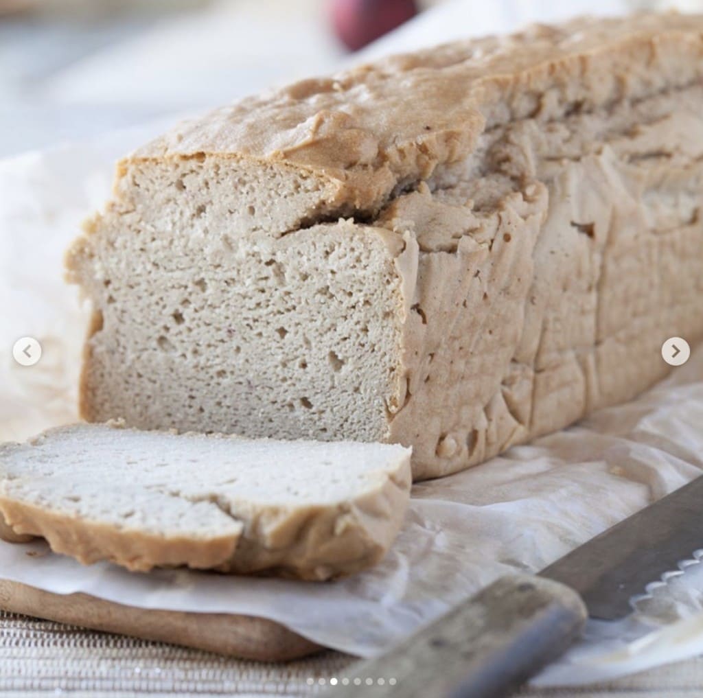 freshly baked loaf of bread with one slice cut off on a wood cutting board next to a bread knife 