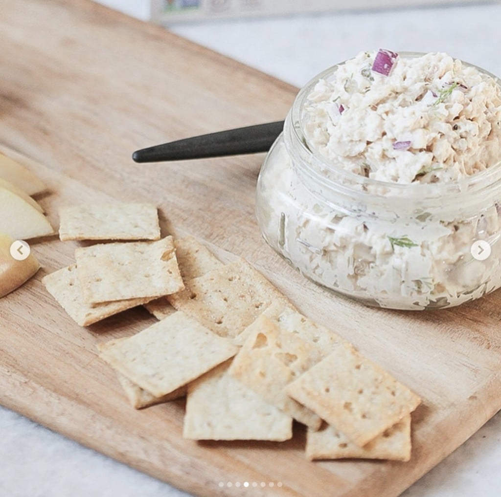 open jar of tuna salad on a wood cutting board with crackers on the side