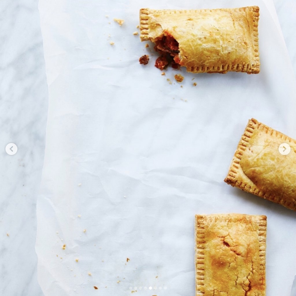 One rectangle shaped pastry with a missing corner piece to show red filling and two others on parchment paper on a white marble counter. 