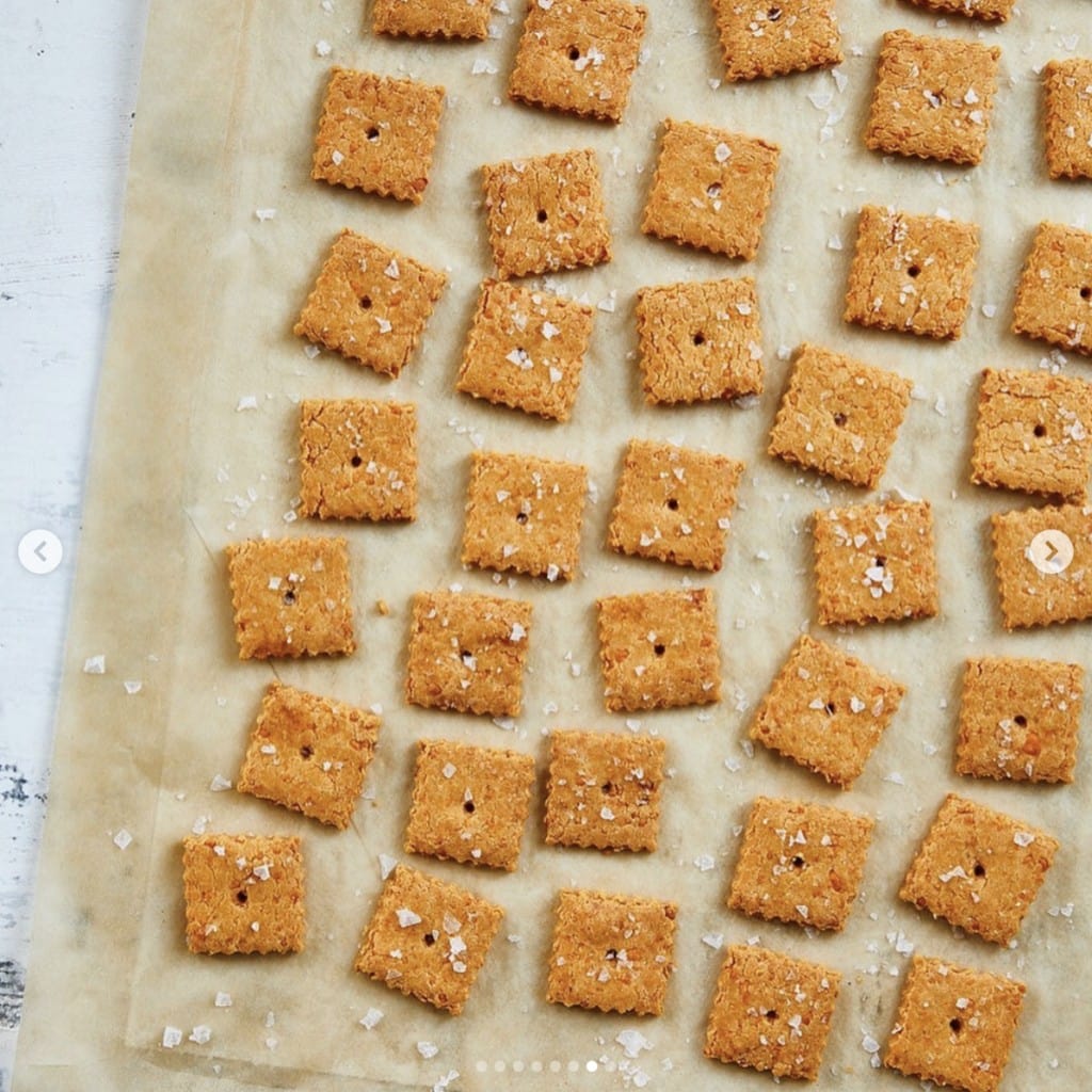 small square orange crackers sprinkled with coarse salt on parchment paper displayed on a white marble counter