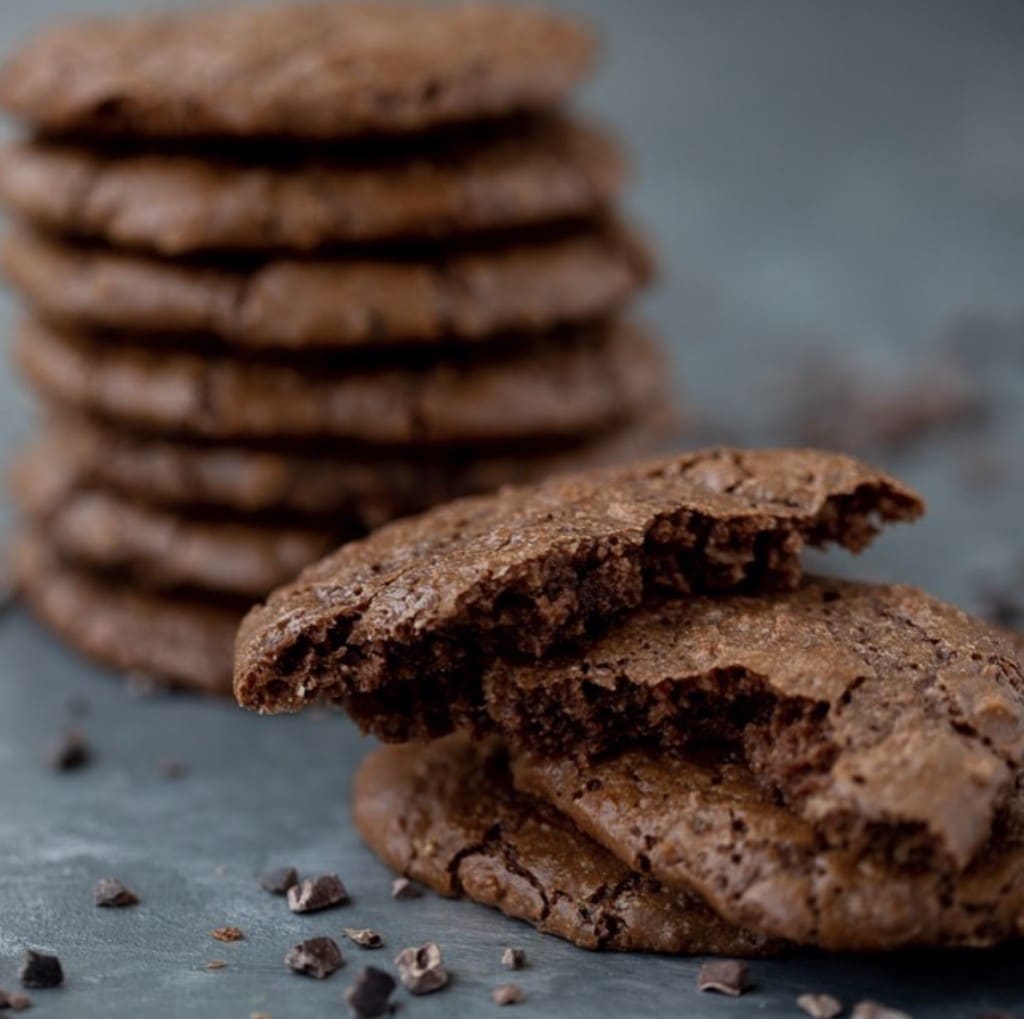 stacks of chocolate cookies displaying crinkle texture surrounded by cacao nibs displayed on a dark gray surface 