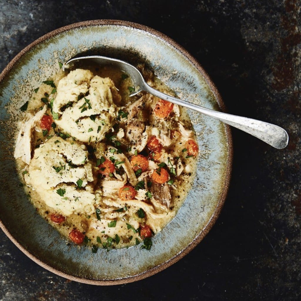 chicken and dumplings in a rustic blue bowl with a silver spoon on a dark gray and black surface