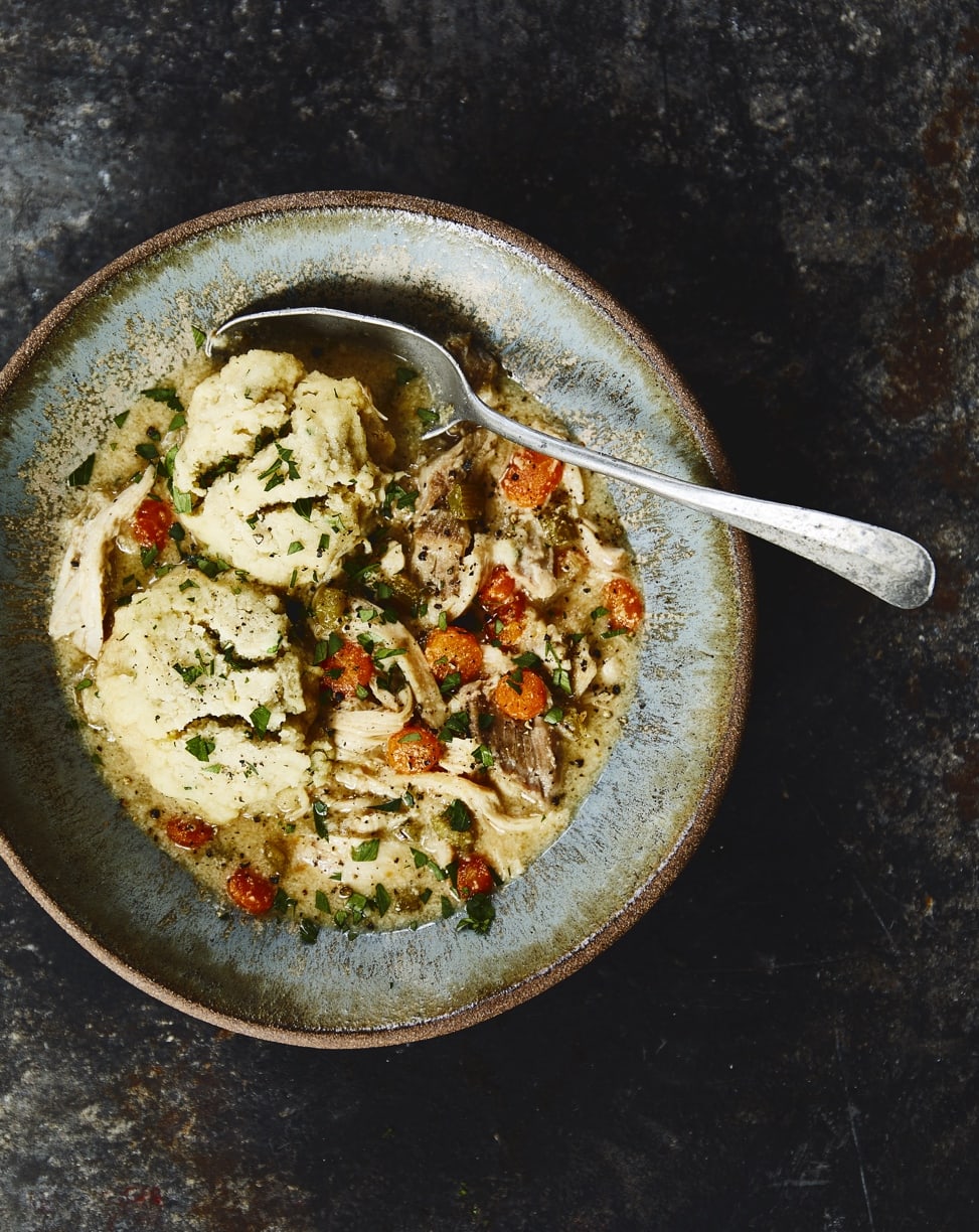 gluten-free Chicken and dumplings with carrots in a light blue rustic bowl with a silver spoon on a dark marbled table