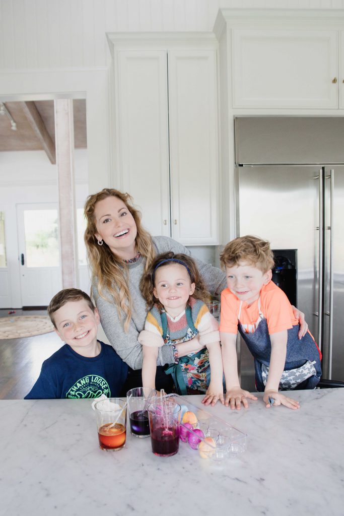 Woman with three children smile while dyeing Easter eggs in home kitchen
