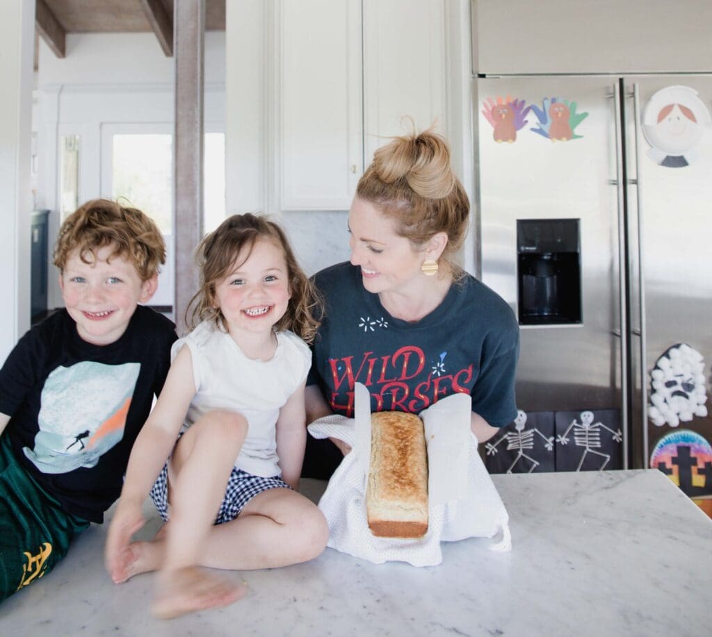 mother holds freshly baked bread while standing in kitchen next to smiling children